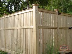 a wooden fence in the middle of some grass and plants next to it is a tall planter