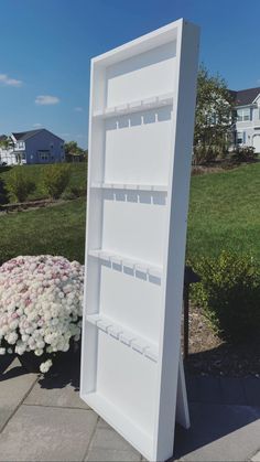 a white book shelf sitting on top of a sidewalk next to a flower pot filled with pink and white flowers