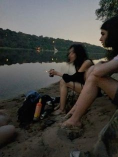 two people are sitting on the beach by the water at night, one is holding a drink