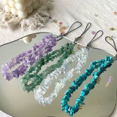 four necklaces are hanging on a mirror with beads and crystals around them, along with confetti