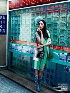 a woman is standing in front of a wall with advertisements on it and talking on her cell phone