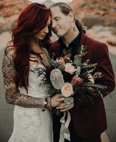 a man and woman standing next to each other with tattoos on their arms holding flowers