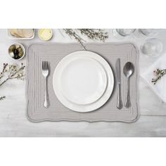 a place setting with white plates and silverware on a gray placemat, surrounded by flowers