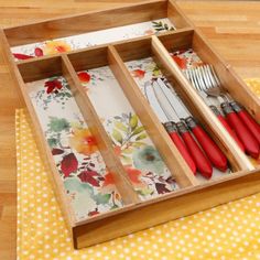 a wooden tray with utensils in it on a yellow and white tablecloth