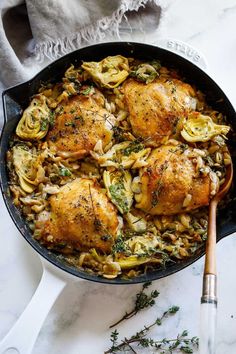 chicken and noodles in a skillet on a marble countertop with a wooden spoon