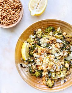 a bowl filled with broccoli and nuts next to a lemon wedge on a table