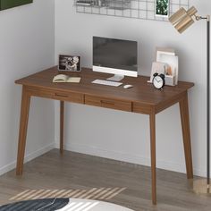 a wooden desk with a computer on top of it next to a lamp and pictures