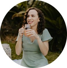 a woman in a green dress holding a wine glass and smiling at the camera while sitting outside