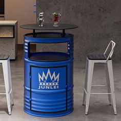 two stools and a table with a blue barrel on it in front of a gray wall