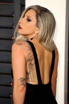 lady with grey hair wearing black dress and tattoos on her back, looking off to the side