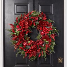 a christmas wreath with red flowers and greenery hangs on a black front door,