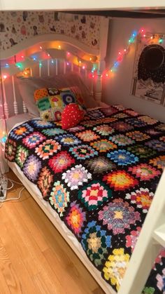 a bed with a colorful quilt on top of it next to a night stand and lights