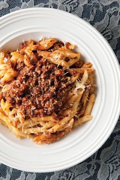 a white plate topped with pasta covered in meat and sauce on top of a table