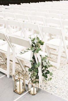 two white chairs with greenery tied to them and some candles on the ground in front of them