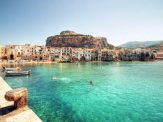 people are swimming in the blue water next to some buildings and boats on the shore