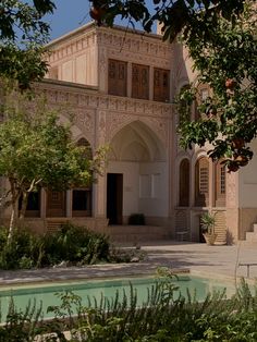 an old building with a fountain in front of it and lots of greenery around the courtyard