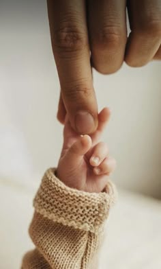 a baby's hand holding the finger of an adult in a knitted sweater