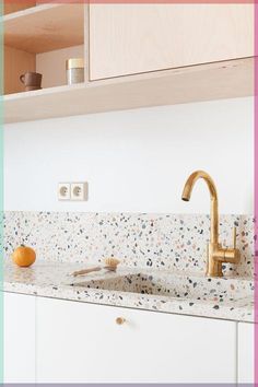 a kitchen with white cabinets and gold faucet on the counter top, next to an orange