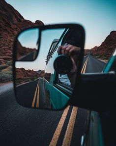 a car's rear view mirror is reflecting the road in it and mountains are seen in the background