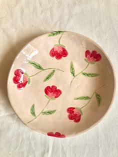 a bowl with red flowers painted on it sitting on a white cloth covered tablecloth