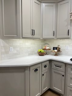 a white kitchen with gray cabinets and marble counter tops on the island in front of the sink