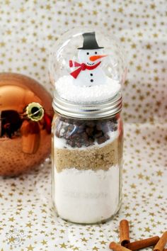 a snowman in a glass jar filled with nuts and spices next to a christmas ornament