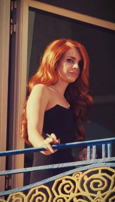 a woman with long red hair standing on a balcony