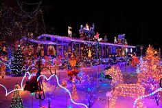 a house covered in christmas lights at night with lots of decorations on the front yard