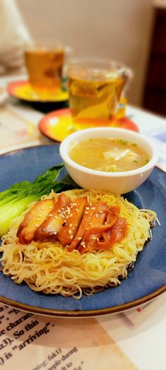 a blue plate topped with noodles and meat next to a bowl of soup on top of a table