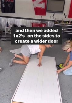 two people laying down on the floor in front of a large piece of plywood