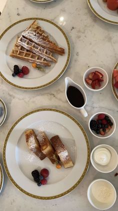 plates with waffles and fruit on them sitting on a marble counter top next to cups