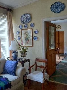 a living room with blue and white plates on the wall next to a chair in front of a door