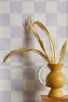 a vase with some dry grass in it on a table next to a checkered wall