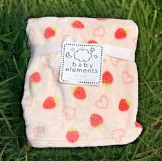 a baby blanket with strawberries on it laying in the grass next to a tag