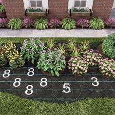 a garden with flowers and numbers painted on the ground in front of a brick building