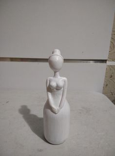 a small white sculpture sitting on top of a table next to a vase with a woman in it