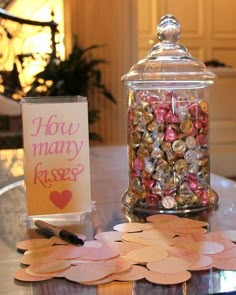 a glass jar filled with lots of candies on top of a table next to a sign that says how many kisses?