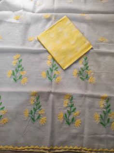 a table cloth with yellow flowers and green leaves on it, next to a napkin