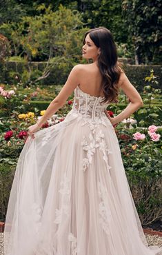 a woman wearing a wedding dress with flowers on the back and in front, looking off to the side