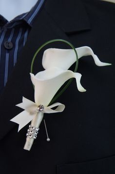 the boutonniere is decorated with white calla lilies and pearls on a black jacket