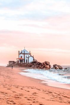 a small white church sitting on top of a sandy beach next to the ocean at sunset