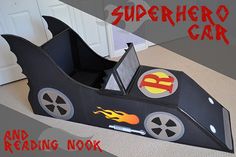 a cardboard race car that is on the floor in front of a door with fire and superman stickers on it