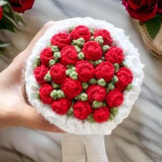 a hand holding a white and red crocheted bowl with flowers in it on a marble surface