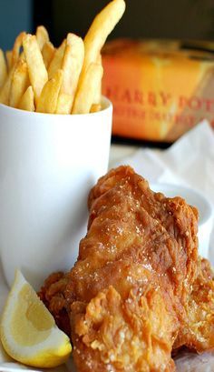 fried chicken and french fries are served in a white bowl with lemon wedges on the side