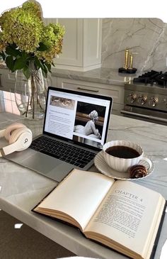 an open book sitting on top of a laptop computer next to a cup of coffee