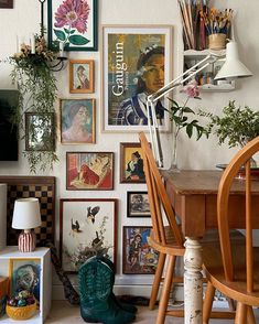 a room filled with lots of pictures and plants next to a wooden table in front of a white wall