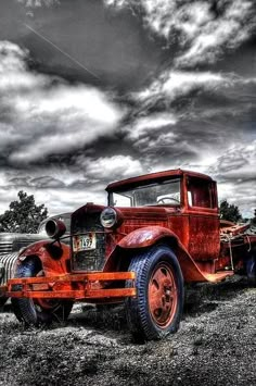 an old red truck parked on top of a grass covered field under a cloudy sky