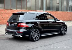 a black mercedes suv parked in front of a brick building on the side of the road