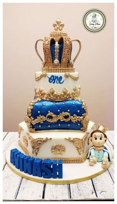 a three tiered cake with blue and gold decorations on top, sitting on a wooden table