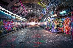 an empty subway tunnel with graffiti all over the walls and floor, along with lights on either side